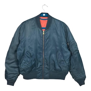 May include: A teal bomber jacket with a contrasting orange lining. The jacket features a zip-up front, two front pockets, and a ribbed collar and cuffs. The jacket is hanging on a metal hanger against a white background.