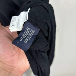 May include: Close-up of a black garment with attached tags. The tags display washing instructions and composition details in both English and French. The garment has a small size label, marked "S".