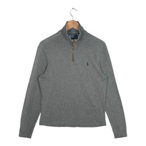 May include: A grey long-sleeved sweatshirt with a quarter-zip closure and a small green logo on the chest. The sweatshirt has a high collar and ribbed cuffs. The zipper is brown. The sweatshirt is hanging on a wooden hanger.