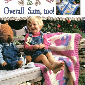 May include: A crochet pattern book featuring a girl sitting on a bench with a teddy bear. The book cover has a title that reads "Sunbonnet Sue & Overall Sam, too!" and a smaller image of a crocheted blanket. The book is designed by Ramona B. Chebli.
