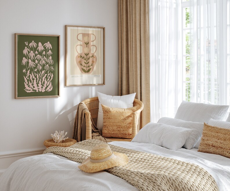 May include: A bedroom with a white bed, a wicker chair, and two framed botanical prints on the wall. The bed has a white duvet, a beige knitted throw, and a straw hat on top. The prints feature a pink flower and a vase with flowers.