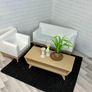 May include: A living room set with a white couch, a white armchair, a beige coffee table, a potted green plant, and two white candle holders on a black rug.