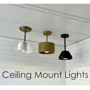 May include: Three ceiling mount lights in gold, tan, and black. The light fixtures have different shapes: a clear dome, a cylinder, and a cone. The text "Ceiling Mount Lights" is displayed below the lights.