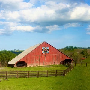 May include: A red barn with a colorful quilt pattern painted on the side. The barn is surrounded by a wooden fence and green grass.