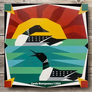 May include: A geometric quilt block design featuring two black and white loons swimming in a turquoise lake with a yellow sun rising behind them. The background is a red and black geometric pattern. The quilt block is signed "Carole Montgomery ©2024".