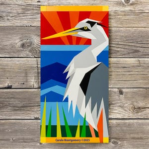 May include: Geometric art print of a heron with a yellow beak and eye, set against a red and orange sunset over blue water and mountains. Green and yellow grass is in the foreground. The artist's name and copyright are at the bottom.