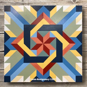 May include: A geometric quilt block with a starburst design in shades of red, yellow, blue, and green. The block is made of wood and painted with a high-gloss finish. The text "Carole Montgomery &copy;2021" is printed in the bottom right corner.