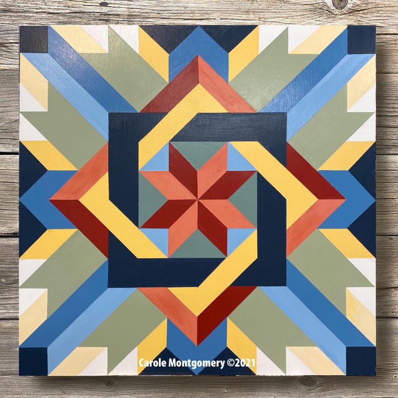 May include: A geometric quilt block with a starburst design in shades of red, yellow, blue, and green. The block is made of wood and painted with a high-gloss finish. The text "Carole Montgomery &copy;2021" is printed in the bottom right corner.