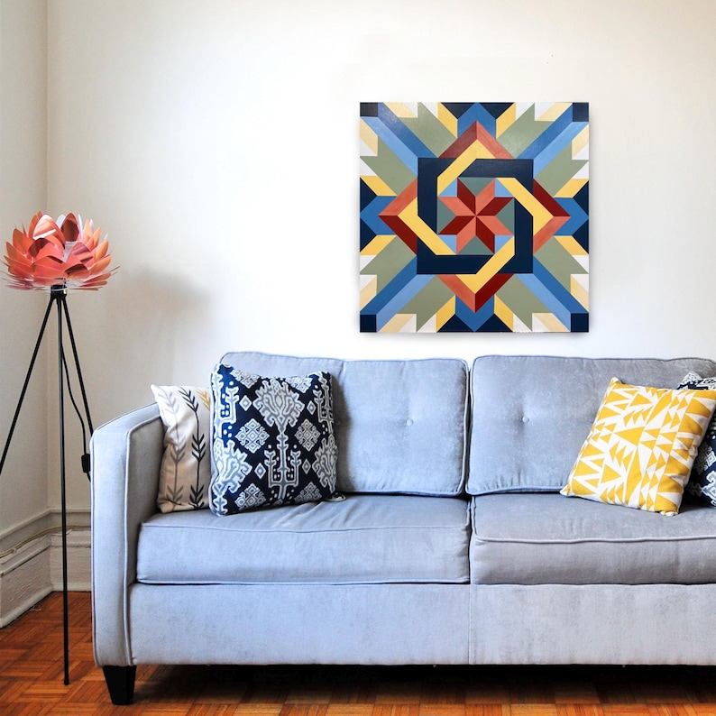 May include: A geometric abstract painting with a swirling pattern in shades of blue, red, yellow, and green. The painting is framed and hanging on a white wall above a light blue sofa.