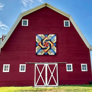 May include: A red barn with a white door and windows. The barn has a large painted design on the side, featuring a colorful geometric pattern.