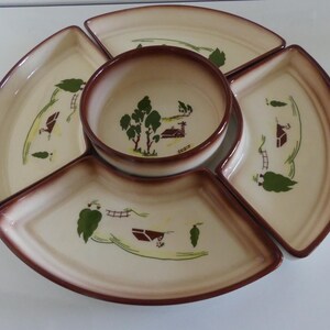 May include: A vintage ceramic serving dish with a central bowl and five surrounding sections. The dish features a cream-colored interior with a brown rim and a rural landscape design in green and brown.