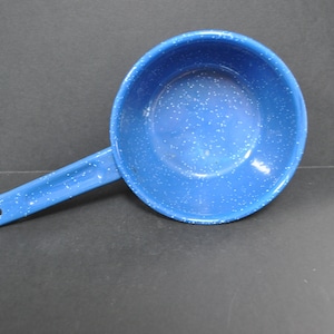 May include: A blue enamelware saucepan with a long handle and a speckled pattern. The saucepan is a vibrant blue with white speckles, and it has a single handle with a hole at the end for hanging. This camping cookware is ideal for outdoor cooking.