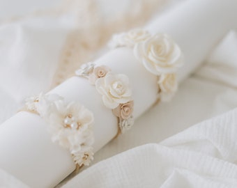 May include: Three white floral headbands with pearl accents. The headbands are arranged on a white surface.