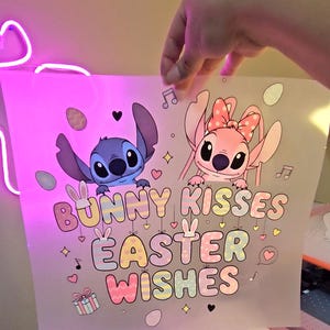 May include: A print featuring the characters Stitch and Angel from Lilo & Stitch. The design includes the text "Bunny Kisses Easter Wishes" in pastel colors, along with Easter-themed illustrations like eggs and musical notes.