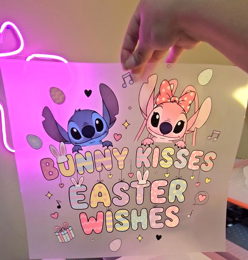 May include: A print featuring the characters Stitch and Angel from Lilo & Stitch. The design includes the text "Bunny Kisses Easter Wishes" in pastel colors, along with Easter-themed illustrations like eggs and musical notes.