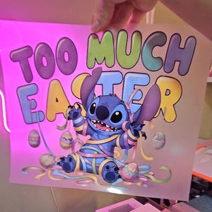 May include: A colorful graphic featuring the character Stitch from Lilo & Stitch, wrapped in pastel ribbons and surrounded by Easter eggs. The text "TOO MUCH EASTER" is displayed in large, playful letters above the character.
