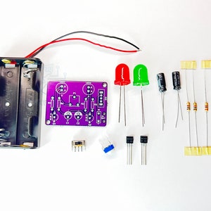 Puede incluir: Una placa de circuito impreso de color morado con varios componentes electrónicos, incluyendo dos LED, dos transistores, dos condensadores, tres resistencias, un interruptor y un soporte para baterías.