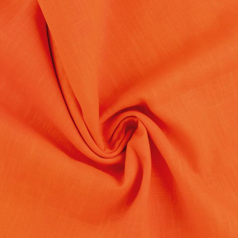 Op de afbeelding: Close-up van een feloranje stof met zichtbare textuur en plooien. Het materiaal lijkt lichtgewicht, mogelijk linnen of een vergelijkbaar geweven textiel. De heldere kleur suggereert dat het gebruikt kan worden voor kleding of woondecoratie.