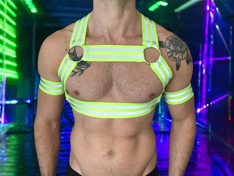 Made-to-measure men’s elastic chest harness in high-visibility neon yellow with reflective detailing, glowing under blacklight. The design features double shoulder and chest straps joined by circular O-rings, with optional matching jockstrap and thigh bands—ideal for clubwear, festivals, or fetish fashion.