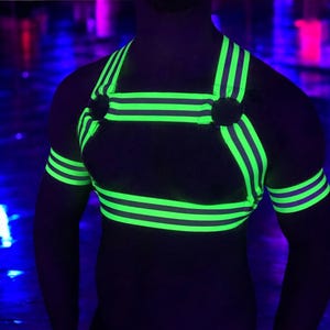 Made-to-measure men’s elastic chest harness in high-visibility neon yellow with reflective detailing, glowing under blacklight. The design features double shoulder and chest straps joined by circular O-rings, with optional matching jockstrap and thigh bands—ideal for clubwear, festivals, or fetish fashion.