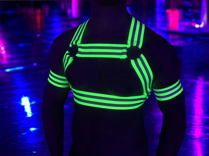 Made-to-measure men’s elastic chest harness in high-visibility neon yellow with reflective detailing, glowing under blacklight. The design features double shoulder and chest straps joined by circular O-rings, with optional matching jockstrap and thigh bands—ideal for clubwear, festivals, or fetish fashion.