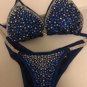 May include: A navy blue bikini with crystal embellishments. The bikini top has a halter style and the bottom is a classic cut.