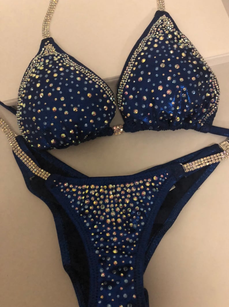 May include: A navy blue bikini with crystal embellishments. The bikini top has a halter style and the bottom is a classic cut.