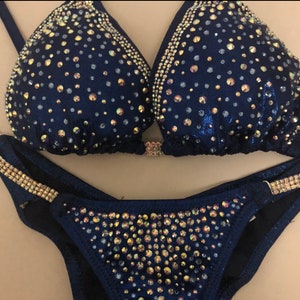 May include: A navy blue bikini with gold and iridescent rhinestones. The bikini top has a halter style and the bottom is a classic cut.