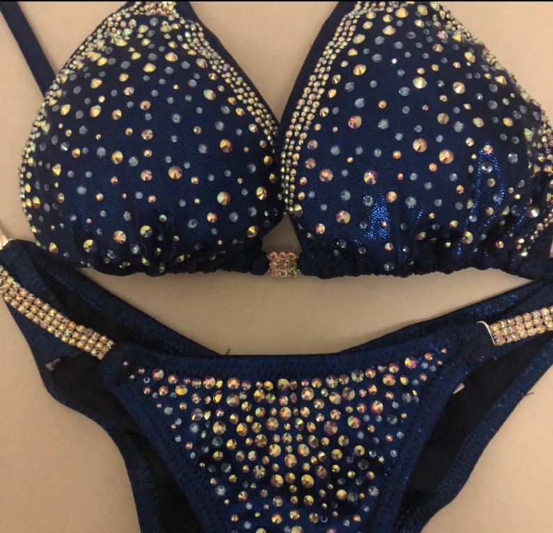 May include: A navy blue bikini with gold and iridescent rhinestones. The bikini top has a halter style and the bottom is a classic cut.