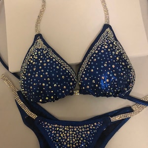 May include: A navy blue bikini with crystal embellishments. The bikini top has a halter style with adjustable straps. The bikini bottom has a high-cut style.