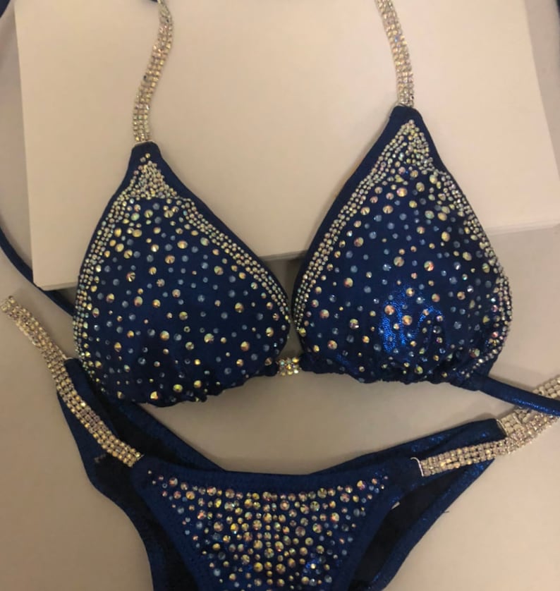 May include: A navy blue bikini with crystal embellishments. The bikini top has a halter style with adjustable straps. The bikini bottom has a high-cut style.