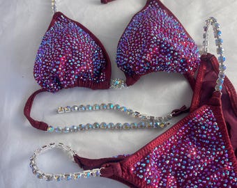 Puede incluir: Bikini burdeos con adornos de cristal. La parte superior del bikini tiene un estilo halter con cierre de broche en la parte delantera. La parte inferior del bikini tiene un estilo de corte alto con un cordón de amarre a cada lado.