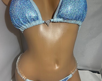 May include: A light blue bikini with crystal embellishments. The top has a halter style with a clasp closure in the front. The bottom has a low-rise cut with a crystal-encrusted strap on each side.