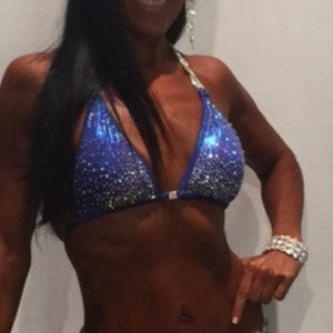 May include: A woman wearing a blue and silver sequined bikini with rhinestones. She is posing for a competition and has a number "220" on her bikini bottom.