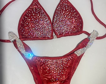 May include: A red bikini with crystal embellishments. The top has a halter style and the bottom has a high-cut leg.