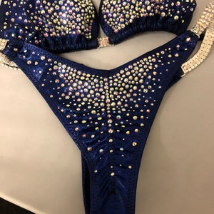 May include: A navy blue swimsuit with iridescent rhinestones. The swimsuit has a halter top and a high-cut bottom.