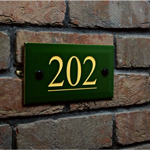 Könnte beinhalten: Ein grünes Hausnummernschild mit goldenen Buchstaben, die Nummer 202 ist auf dem Schild angezeigt.