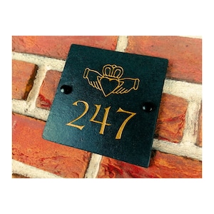 May include: Black slate house number sign with gold lettering. The number 247 is displayed on the sign. A Celtic knot design with a heart is above the number.