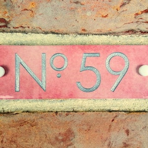 May include: A pink ceramic house number plaque with white dots on either side. The number "No. 59" is written in silver lettering.