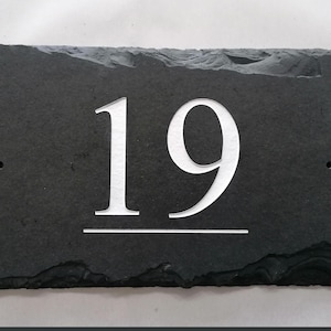 Può includere: Un cartello per numeri civici in ardesia nera con il numero 19 inciso in bianco.