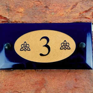 May include: A blue and gold house number sign with the number 3 and Celtic knot designs.