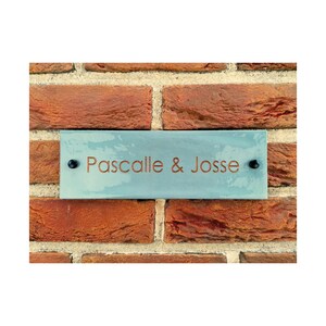May include: A light blue rectangular sign with black screws and the text "Pascalle & Josse" in copper lettering.