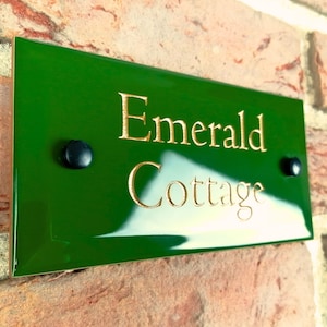 May include: A green house number sign with gold lettering that reads "Emerald Cottage".