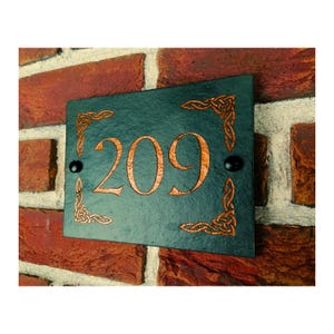 May include: A dark green slate house number sign with a copper Celtic knot design and the number 209 in copper.