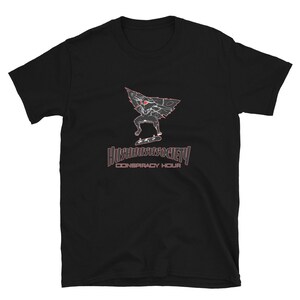Puede incluir: Camiseta negra con un gráfico de una criatura con ojos rojos haciendo skateboard y el texto "Hushhushsociety Conspiracy Hour".