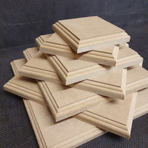 May include: A stack of six unfinished wooden square plaques with a decorative edge. The plaques are arranged in a pyramid shape.