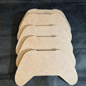 May include: Four unfinished wooden game controller shapes stacked on top of each other. The shapes are light brown and have a smooth surface.