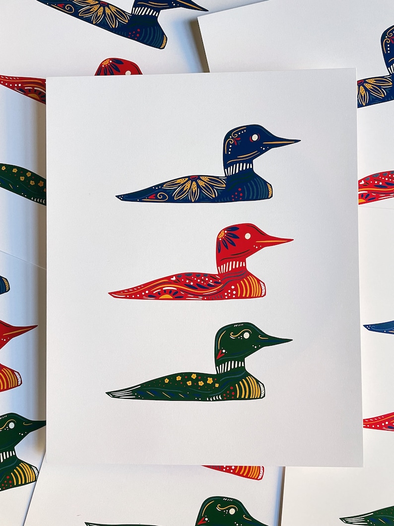 May include: A set of three colorful loon prints. The loons are depicted in a folk art style with intricate patterns and bright colors. The loons are in red, blue, and green.