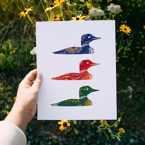 May include: A white card with three colorful loon illustrations. The loon on the top is blue with white and yellow accents. The middle loon is red with white and yellow accents. The bottom loon is green with white and yellow accents.