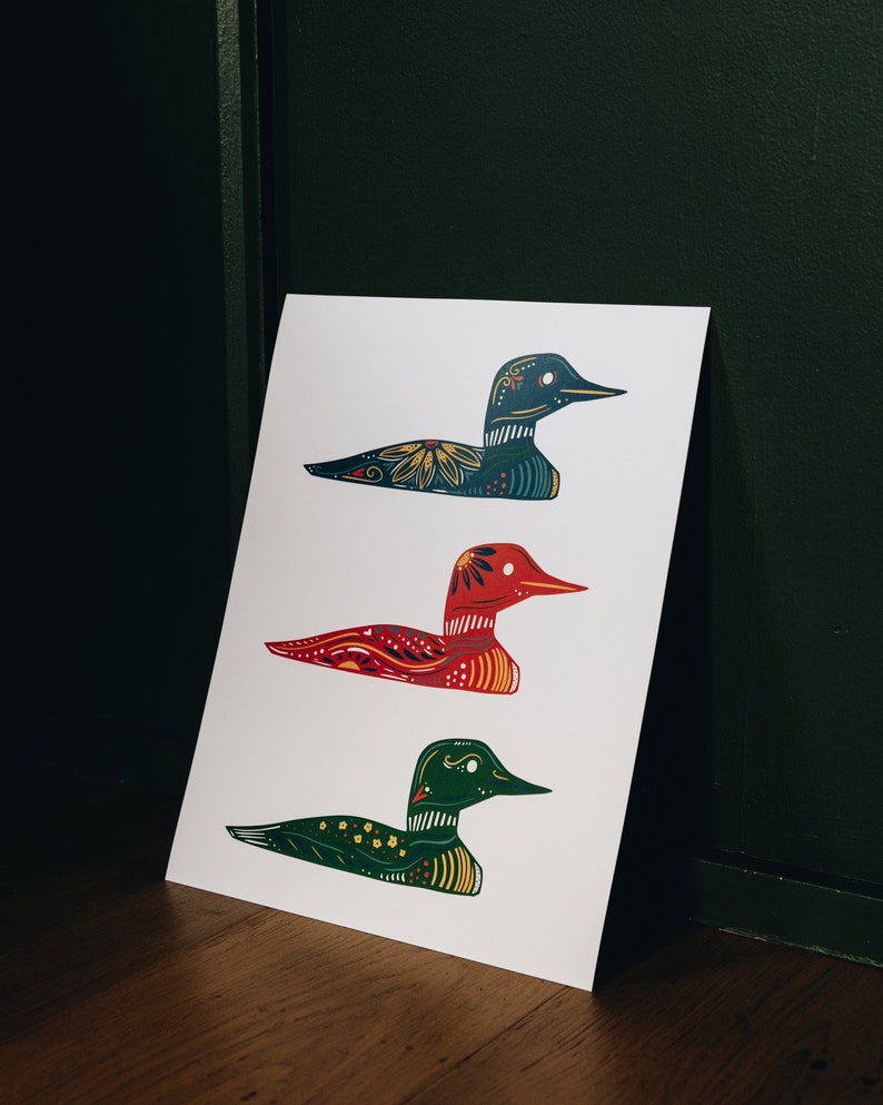 May include: Three colorful loon bird illustrations on a white background. The top loon is teal blue with yellow and red accents. The middle loon is red with yellow and black accents. The bottom loon is green with yellow and red accents.